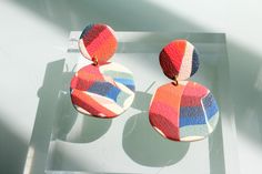 two pairs of multicolored earrings sitting on top of a glass table next to each other