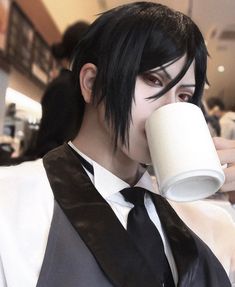 a man with black hair drinking from a cup