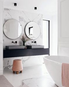 a bathroom with marble walls and flooring, two round mirrors on the wall above the sink