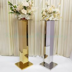 two tall vases with flowers in them sitting on a white tablecloth covered floor