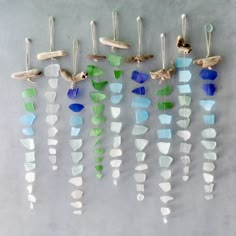 several pieces of sea glass hanging from hooks on a gray wall with birds and seashells attached to them