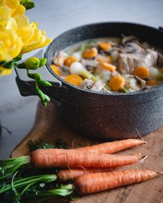 carrots and mushrooms are on a cutting board next to a pot with soup in it