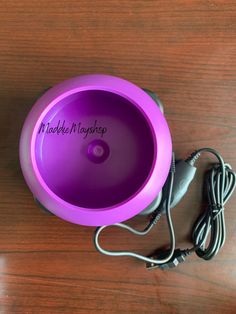 a purple speaker sitting on top of a wooden table next to a corded charger