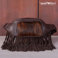 Made of PU leather, this belt bag has:- Genuine hair-on cowhide Fringe Zip around closure A zipper pocket on the front Inside bag has a zipper pocket and 3 card slots A zipper pocket on the back Trinity Ranch logo patch on the back Adjustable strap 9.5" x 2.5" x 6"（Drop 19.5''） Cow hide upper is natural and will wear under normal conditions. Each bag will vary slightly as each pelt will have a unique pattern. NO TWO BAGS WILL BE EXACTLY THE SAME AND MAY VARY FROM THE PHOTOGRAPHS. Brown Leather Shoulder Bag With Zipper Pouch, Brown Leather Belt Bag With Zipper Closure, Brown Pouch Belt Bag With Zipper, Brown Belt Bag With Zipper Pouch, Ranch Logo, Fringe Belt, Fringed Belt, Inside Bag, Cow Hide