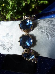 A truly eye-catching and elegant vintage piece in beautiful condition with an amazing sparkle! Beautiful and unique one-of-a kind design. The rhinestone bracelet is made up of eight blue topaz round cut faceted stones that measure 5/8", approximately the size of a dime. They are set in a goldtone metal surrounded at the base with small purple rhinestones.  The stones are securely set in a goldtone metal setting with no loose or missing stones. All have a brilliant sparkle! Will be packaged in a lovely blue velvet gift box as shown and ready for gift giving. For other vintage jewelry listings please visit:  https://www.etsy.com/shop/DreamofjeanieDesigns?ref=seller-platform-cnav&section_id=23284464 Vintage Jewelry With Sparkling Stones For Party, Vintage Sparkling Stones Jewelry For Party, Glamorous Round Jeweled Jewelry, Vintage Party Jewelry With Sparkling Stones, Glamorous Jeweled Jewelry, Blue Crystal Bracelets For Formal Occasions, Elegant Sapphire Crystal Bracelets, Elegant Jeweled Sapphire Jewelry, Elegant Sapphire Jeweled Jewelry