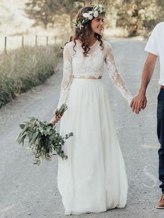 a bride and groom holding hands while walking down a dirt road with greenery in their hair