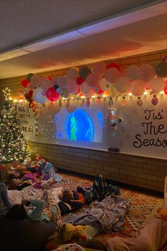 a group of people laying on the floor in front of a christmas tree with balloons