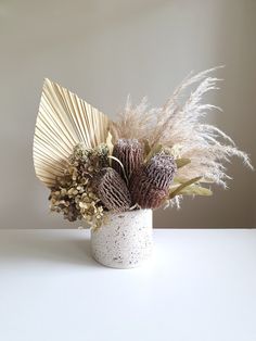 a white vase filled with lots of different types of flowers and plants on top of a table