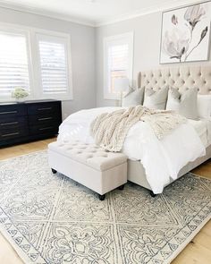 a large bed sitting on top of a wooden floor next to a white dresser and window