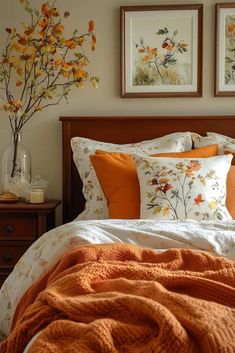 a bed with orange and white pillows in a bedroom next to two framed pictures on the wall