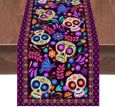 a colorful table runner with skulls and flowers on the border, in front of a wooden surface