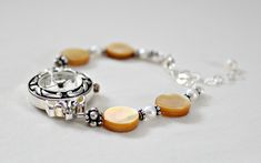 "Mother of pearl sterling silver bracelet watch is handcrafted. Would make a great 50th birthday gift for Mom or Mothers Day gift from son or daughter! Beige shell mother of pearl showcased with white freshwater pearls and Bali sterling silver. Watch is adjustable from 6 1/4\" to 8 1/2\". Metaphysical meaning of Mother of Pearl: Mother of Pearl, considered a protection stone, is a stress relieving stone; relaxing, soothing and calming to the emotions. It stimulates our intuition, imagination, se Timeless Round Pearl Bracelet As Gift, Timeless Silver Pearl Jubilee Bracelet, Elegant Nickel-free Watches As Gifts, Timeless Pearl Oyster Bracelet As Gift, Handmade Silver Pearl Bracelet Gift, Vintage Silver Pearl Bracelet Gift, Silver Pearl Jubilee Bracelet For Anniversary, Handmade Round Pearl Bracelet For Anniversary, Handmade Pearl Bracelet For Anniversary