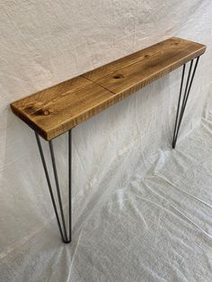 a wooden bench with hairpint legs on a white sheeted background in front of a wall