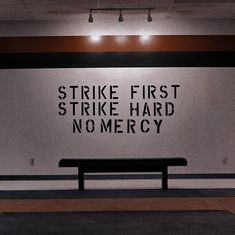 a black bench sitting in front of a wall with words on it that read strike first strike hard nomercy