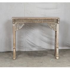 an old wooden table with carvings on the top and bottom, against a white wall