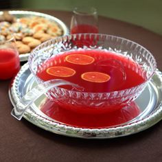 red liquid in a glass bowl on a table with cookies and desserts behind it