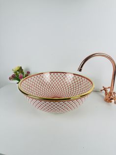 a red and white bowl sitting next to a faucet