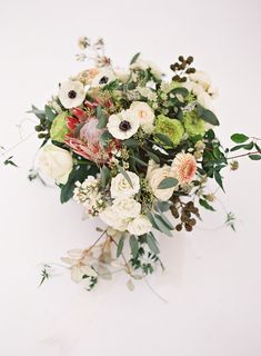 a bouquet of white and green flowers on top of a white surface with greenery