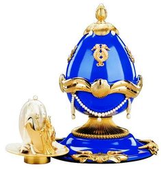 a blue and gold egg sitting on top of a golden stand next to a white background