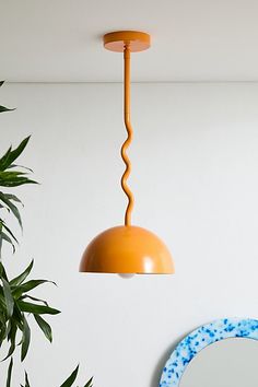 an orange light hanging from a ceiling in a living room with potted plant and mirror