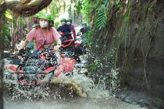 a woman riding on the back of a red four - wheeler through mud and water