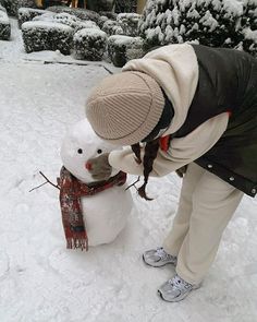 a woman building a snowman outside in the snow