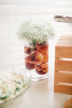 a glass vase filled with flowers and fruit on top of a counter next to a bowl of food