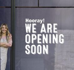 a woman standing in front of a window that says hooray we are opening soon