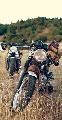 two motorcycles parked in the middle of a field with luggage strapped to them'back