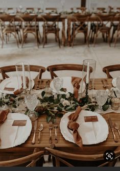 the table is set with white plates and brown napkins, silverware and greenery