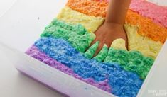 a child's hand on top of a rainbow cake