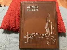 an arizona highway book sitting on top of a bed next to two red throw pillows