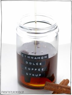 cinnamon coffee syrup being poured into a glass jar with cinnamon sticks in front of it