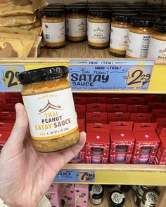 a person holding up a jar of peanut butter in front of shelves with other items