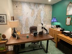 a room with a desk, chair and lamp in it that has a map on the wall