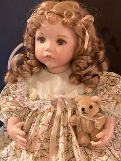 the doll is holding a teddy bear in her hand and wearing a dress with flowers on it