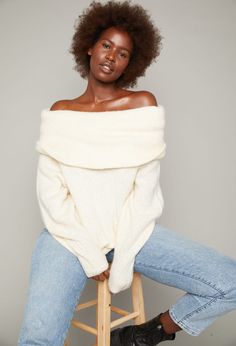 a woman sitting on top of a stool wearing a white sweater and jeans with high heels