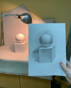 a person holding up a piece of paper with a drawing of a ball and cube on it