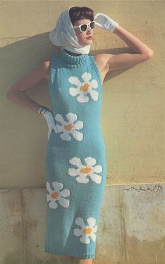 a woman in a blue dress with white flowers on it, leaning against a wall