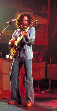 a man with dreadlocks playing an electric guitar in front of a microphone on stage