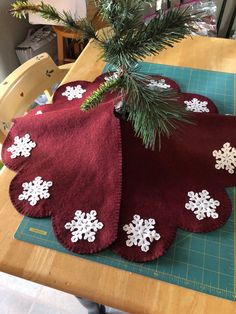 two red towels with white snowflakes are sitting on a cutting board next to a pine tree