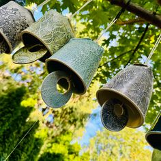 three metal bells hanging from a tree branch in the sun with green leaves behind them