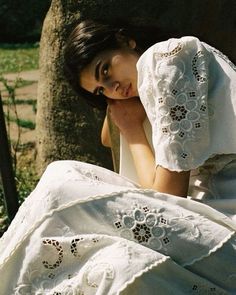 a woman in a white dress sitting under a tree