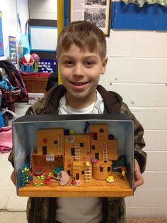 a young boy holding up a cardboard model of a house