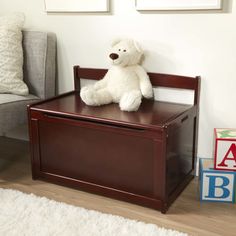 a white teddy bear sitting on top of a wooden toy box next to a couch