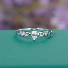 a white gold ring with an oval cut diamond surrounded by vines and leaves on a green surface