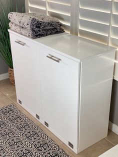 a white cabinet sitting on top of a tiled floor next to a potted plant