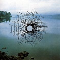 a sculpture is floating in the water with rocks and trees around it, while another piece of wood sticks are sticking out of the water