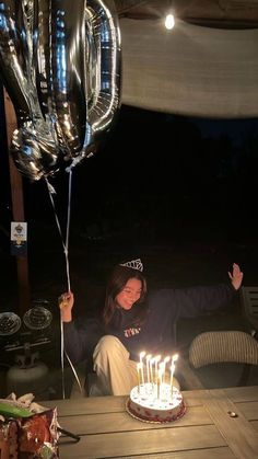 a woman sitting in front of a table with a cake and balloons on top of it