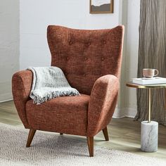 a chair with a blanket on it next to a side table and lamp in a room